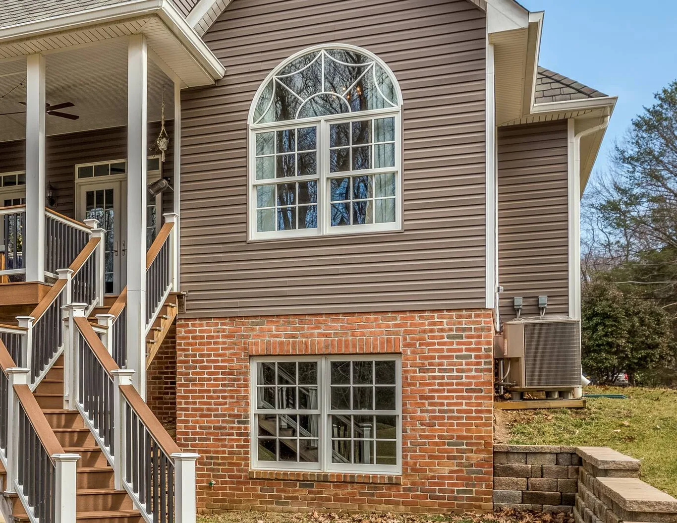 The side of a house with an arched window high in the siding and a grilled window in the brick below