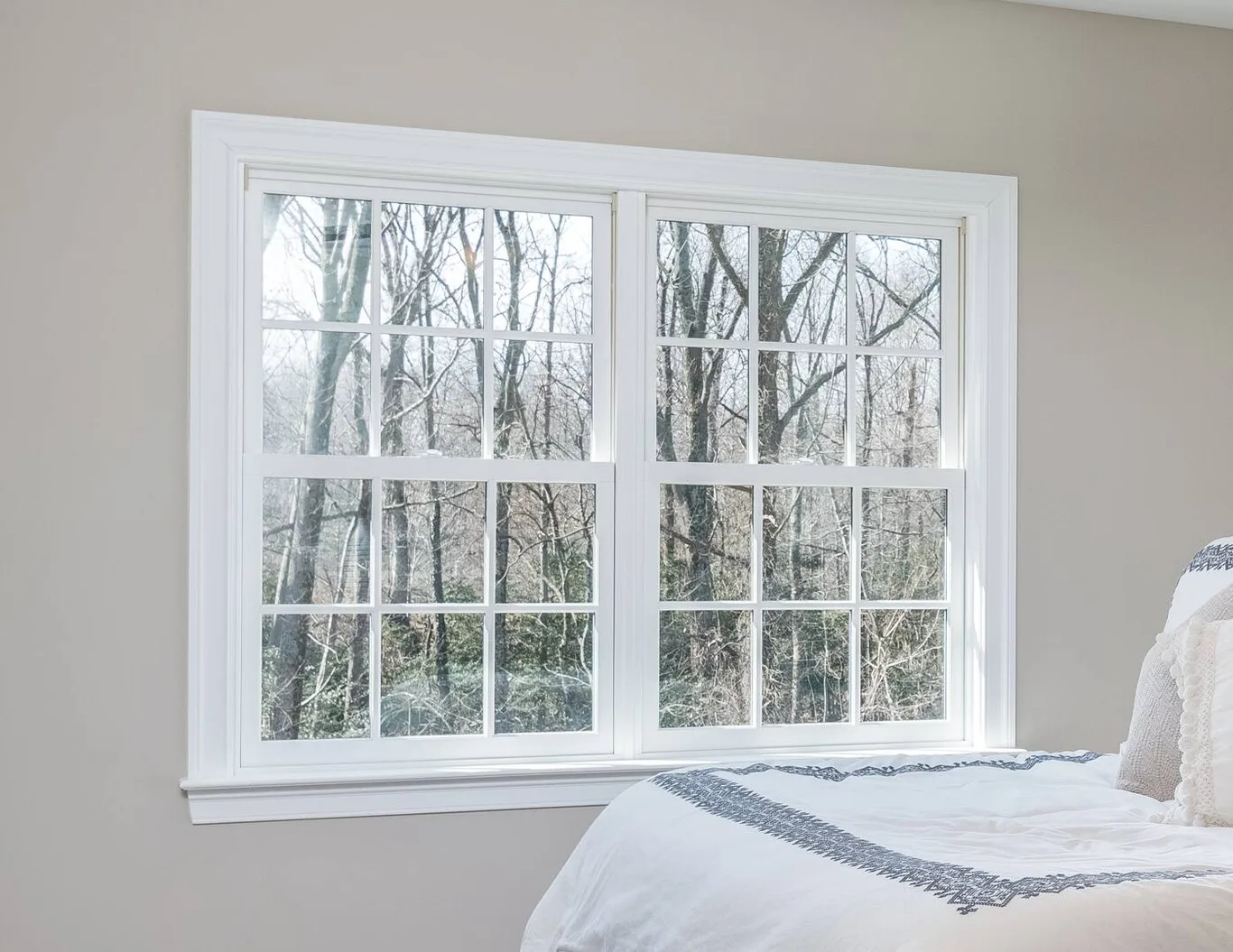 A pair of double-hung windows beside a bed, woods outside