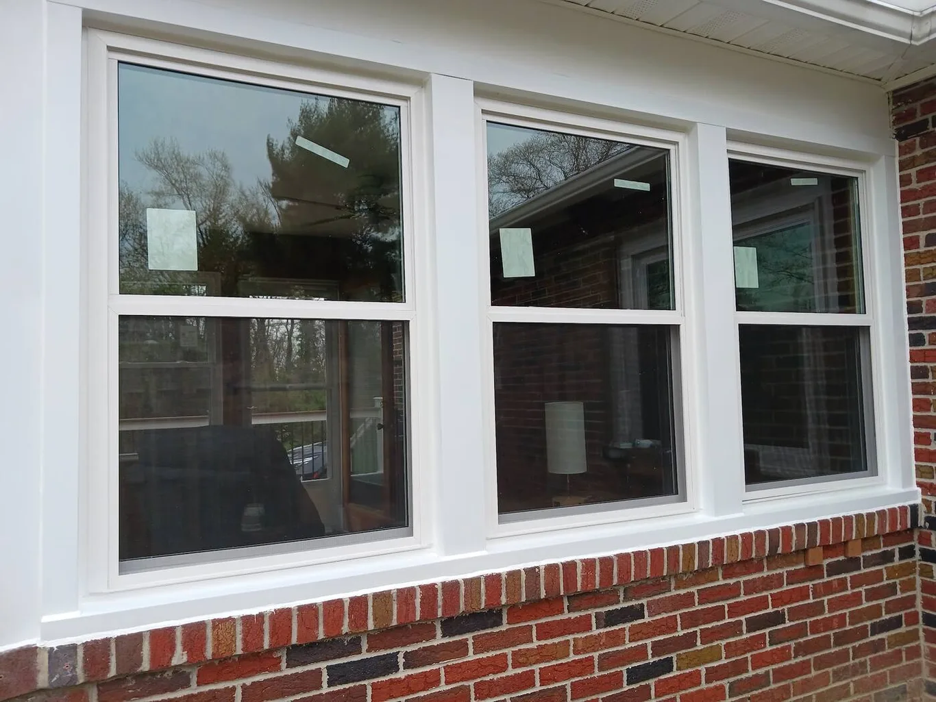 Three new white windows in a row above brick, labels still on the glass