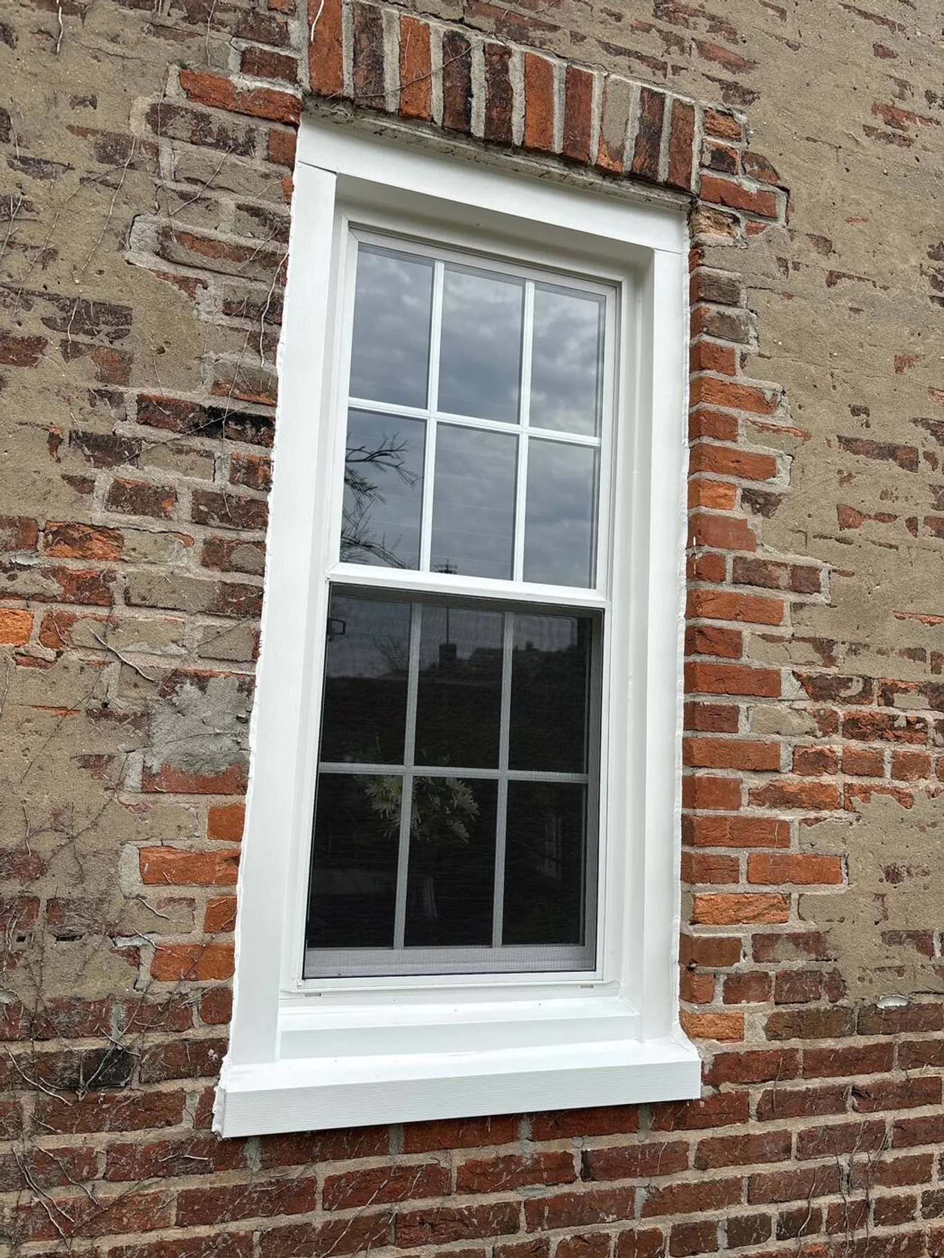 A new six-over-six window in an old, weathered brick wall