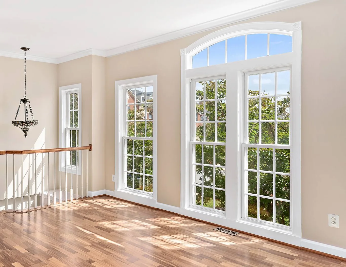 An empty sunlit room with tall grilled windows and an arched transom over the centre pair