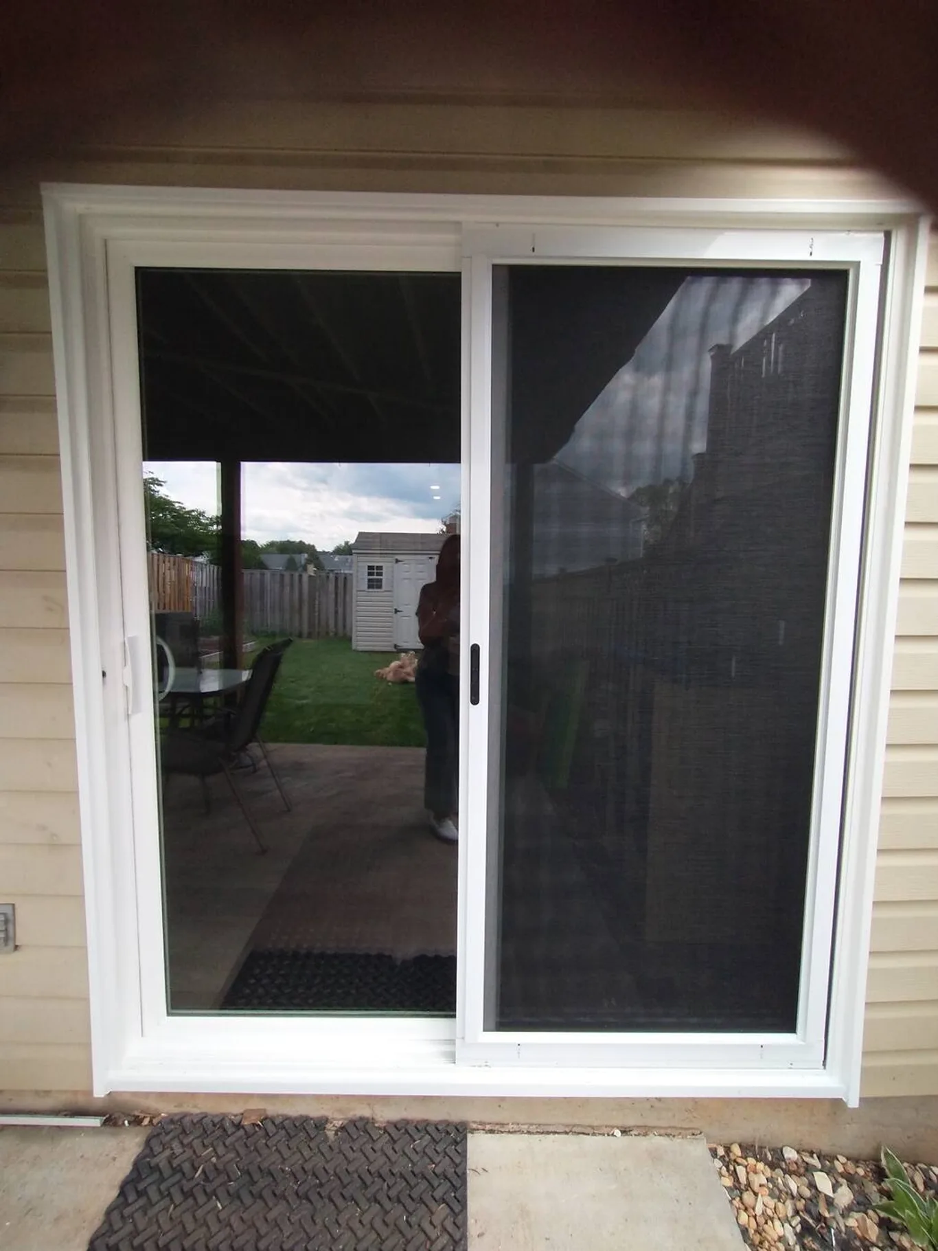 A sliding door from outside, under a porch light, screen panel closed