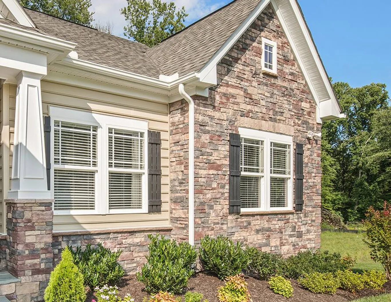 A stone and siding house corner with shuttered double windows