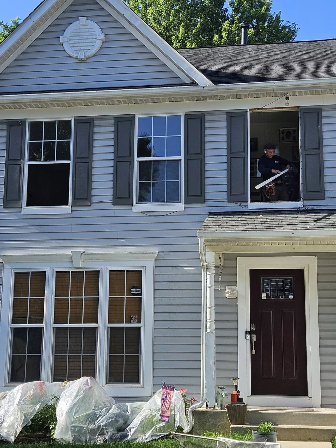 An installer working in an upstairs window opening, the old window out, shutters on either side