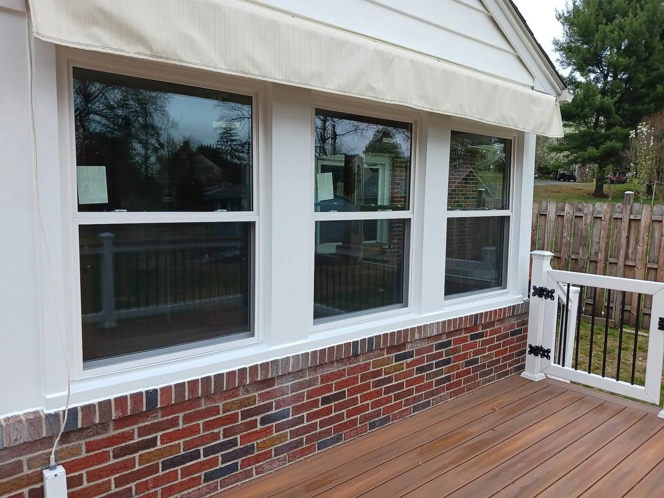 Three large windows above a brick base, beside a new deck