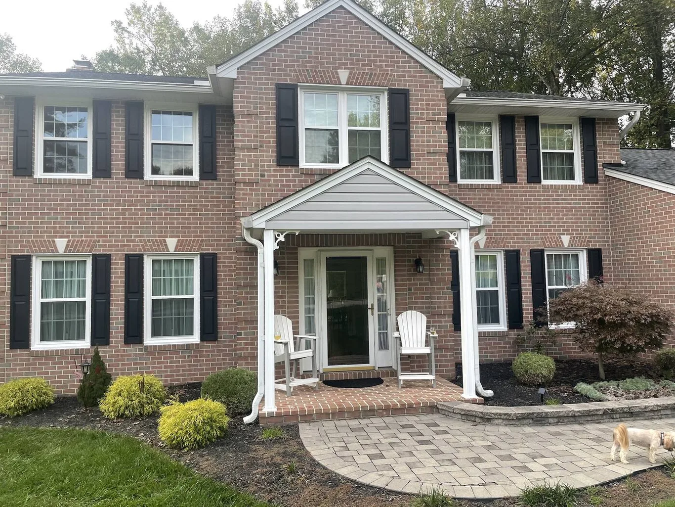 A brick colonial with black shutters and white double-hung windows on both floors