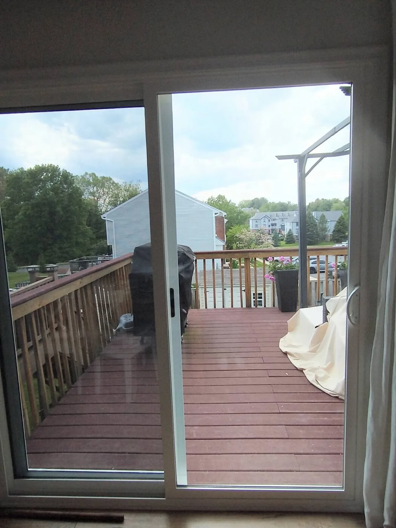 A white-framed sliding glass door, open onto a wooden deck and a backyard
