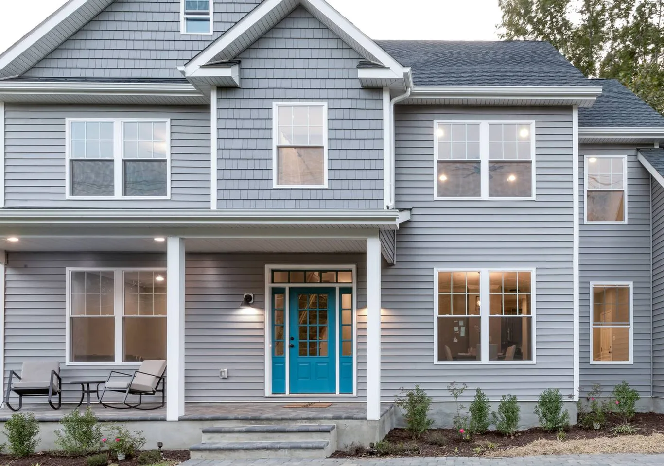 A two-storey house in grey siding with a covered porch, white windows and a teal front door